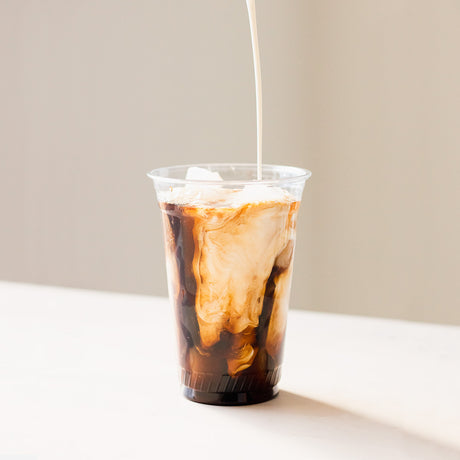 Wholesale clear PET cups filled with iced coffee and cream on a cafe counter